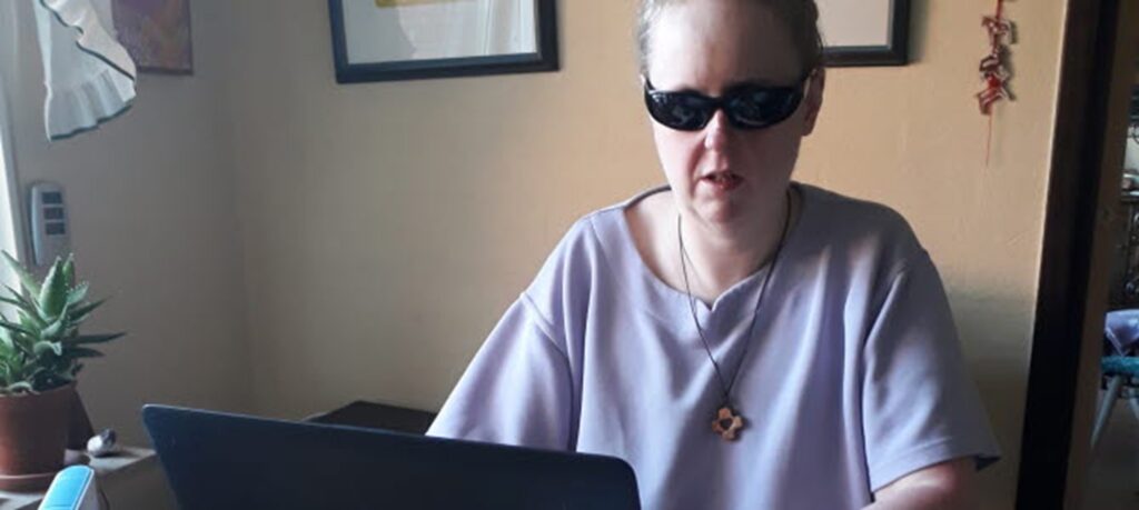 Maria Liesland har blont hår, uppsatt i tofs och mörka solglasögon, hon sitter med en kaffekopp vid sin dator